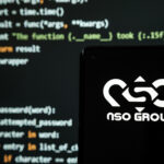 Israel's NSO Group logo seen on smartphone placed in front of laptop with simple hacking code
